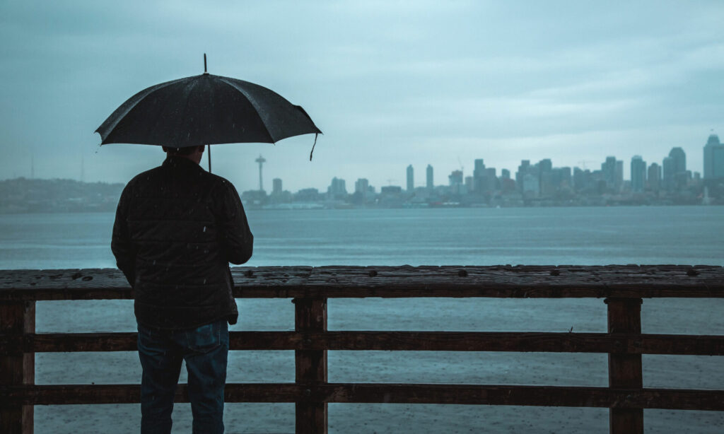 Psychische Gesundheit Mann mit Regenschirm betrachtet die Stadt in der Ferne